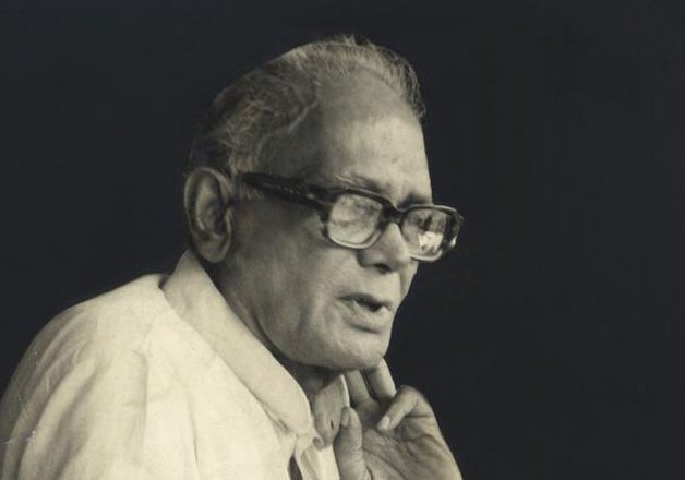 Photograph of Jaya Prakash Narayan in later life, hand raised to his chin, speaking against a dark background